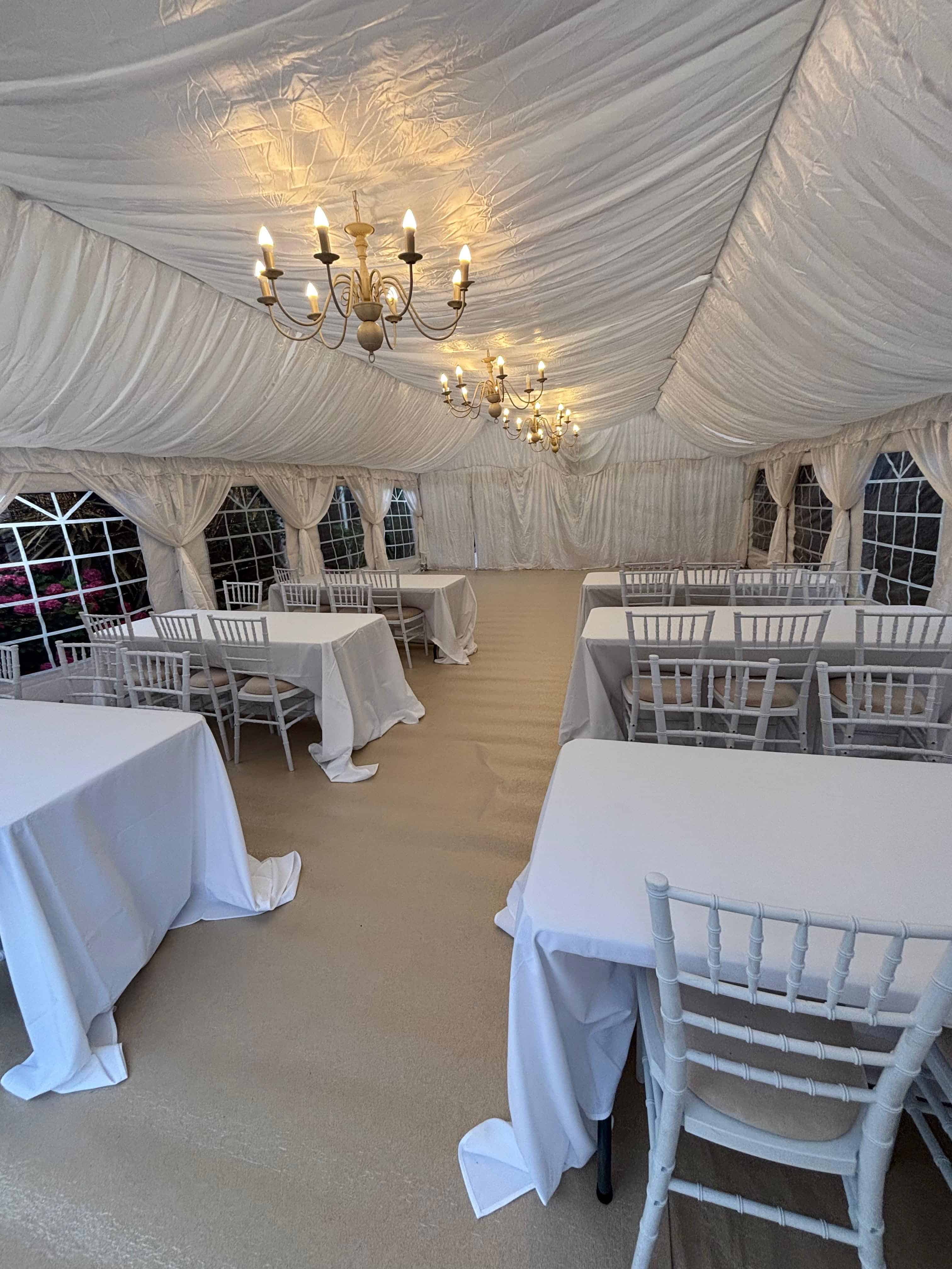 Aisle-down-the-middle event seating with twin chandeliers and white-draped tables in a 6m by 10m marquee
