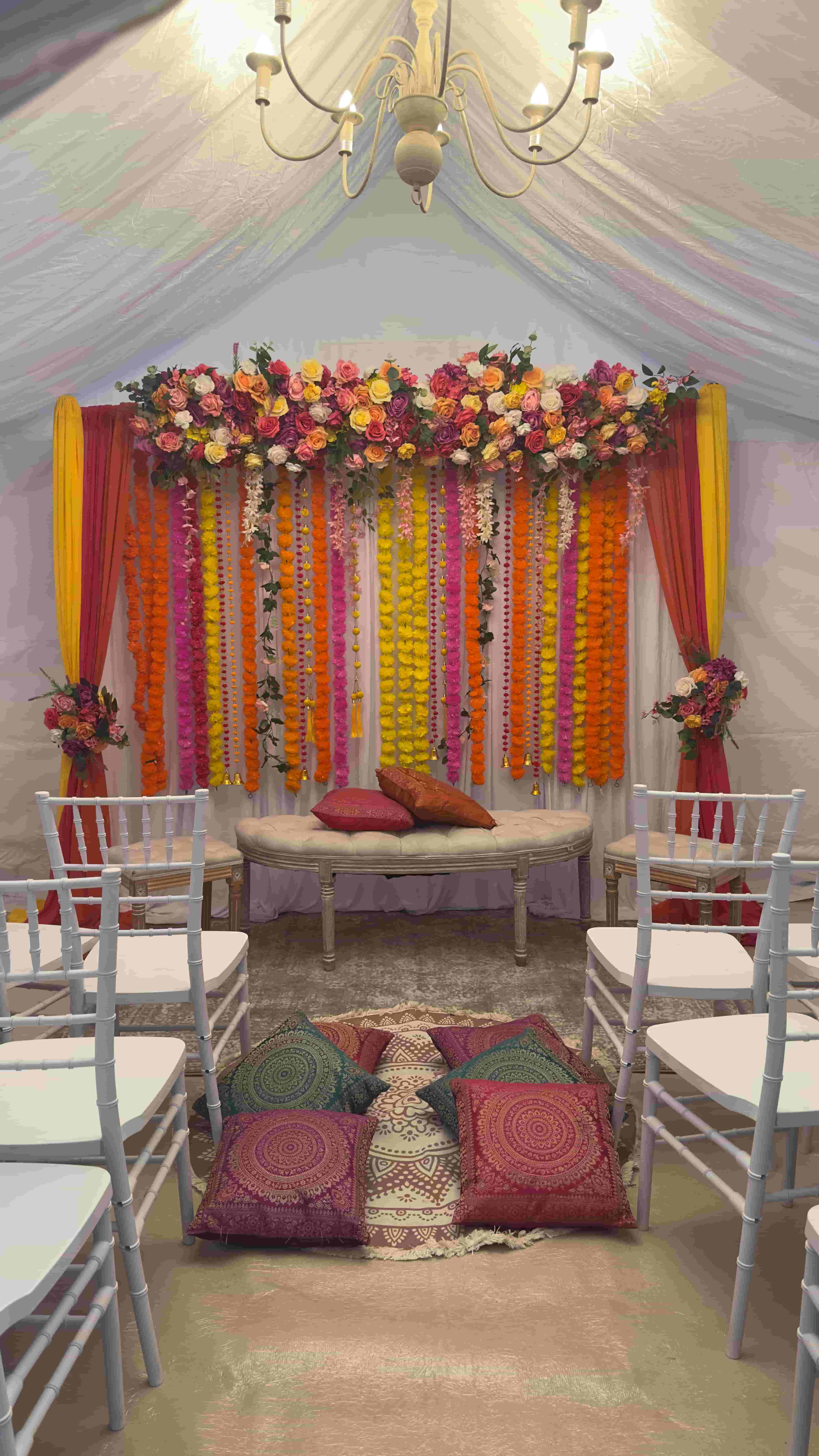 Garland-draped mehndi backdrop with marigold strands and floral arch in a 4m by 4m marquee